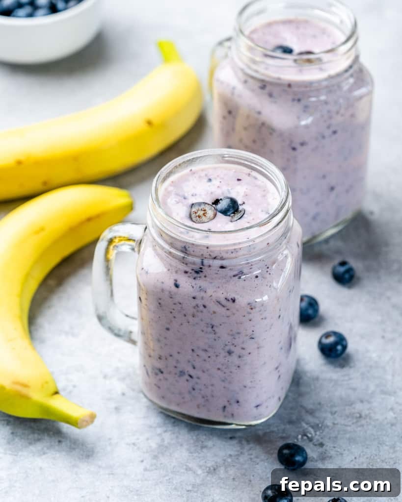 A creamy blueberry banana smoothie in a clear mason jar with a straw, placed on a wooden surface, showcasing its delicious and inviting appearance.