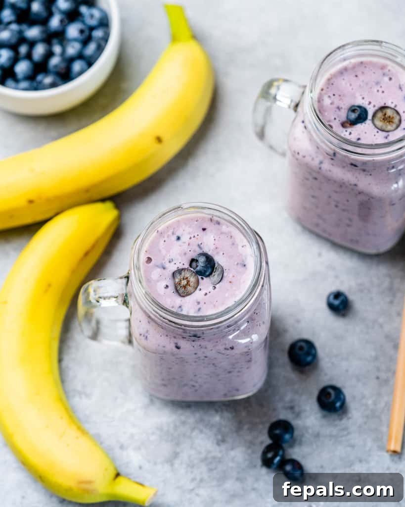 A top-down view of a blueberry banana smoothie in a mason jar with a straw, artfully arranged with fresh banana slices and blueberries on the side, inviting a delightful experience.