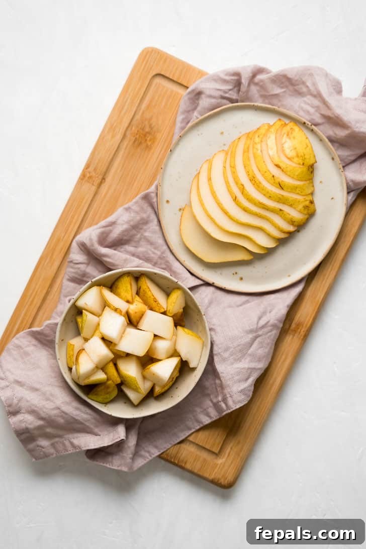 How to Cut a Pear A plate featuring beautifully sliced pears next to a bowl of pear cubes, all arranged on a rustic wooden cutting board with a napkin, ready for serving.