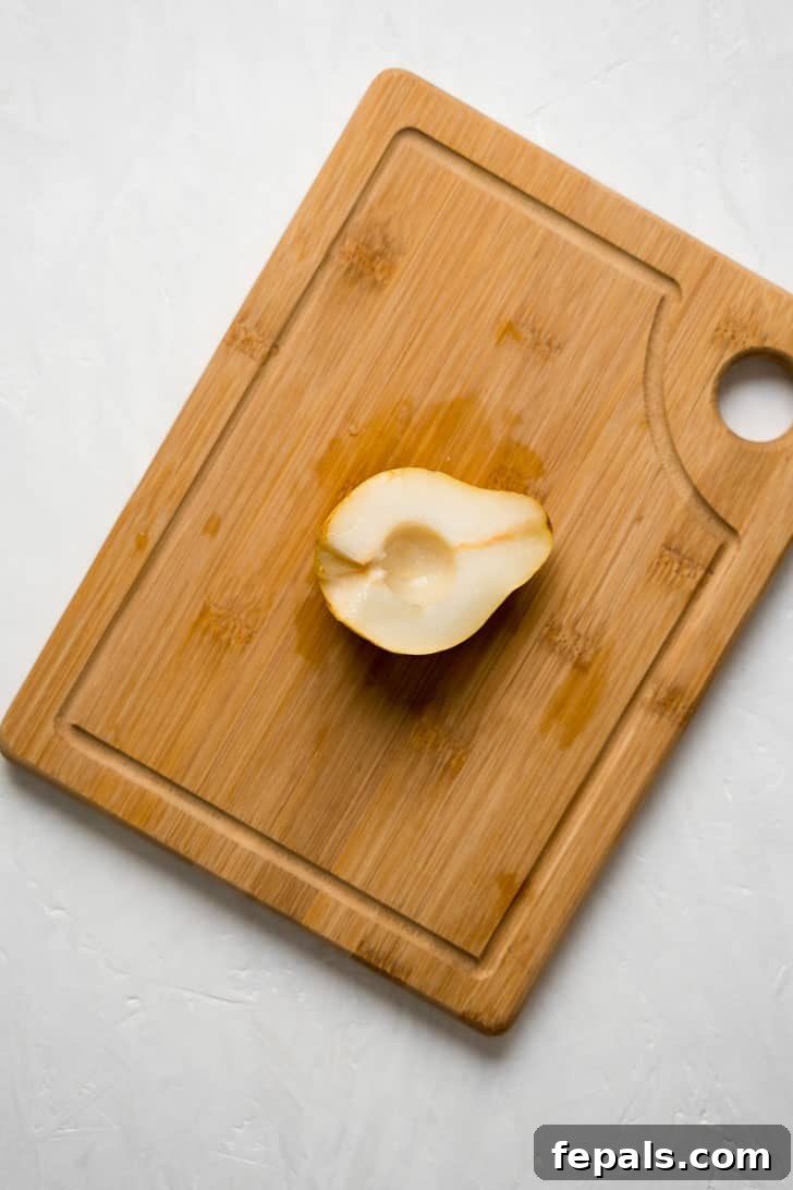 How to Cut and Eat a Pear A perfectly pitted pear half rests on a wooden board, ready for slicing.