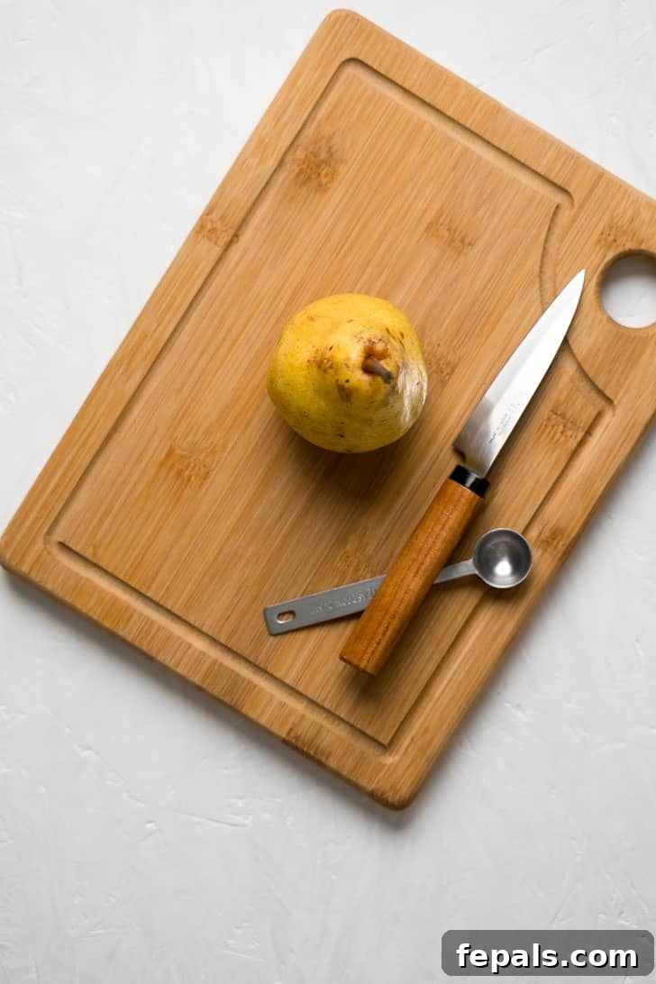 How to Cut a Pear A single pear, positioned on a wooden cutting board, accompanied by a sharp knife and a small spoon, ready for preparation.