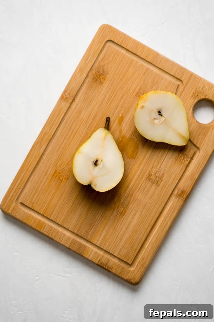 How to Cut a Pear Two halves of a freshly cut pear lie on a wooden cutting board, revealing their juicy interior and ready for coring.