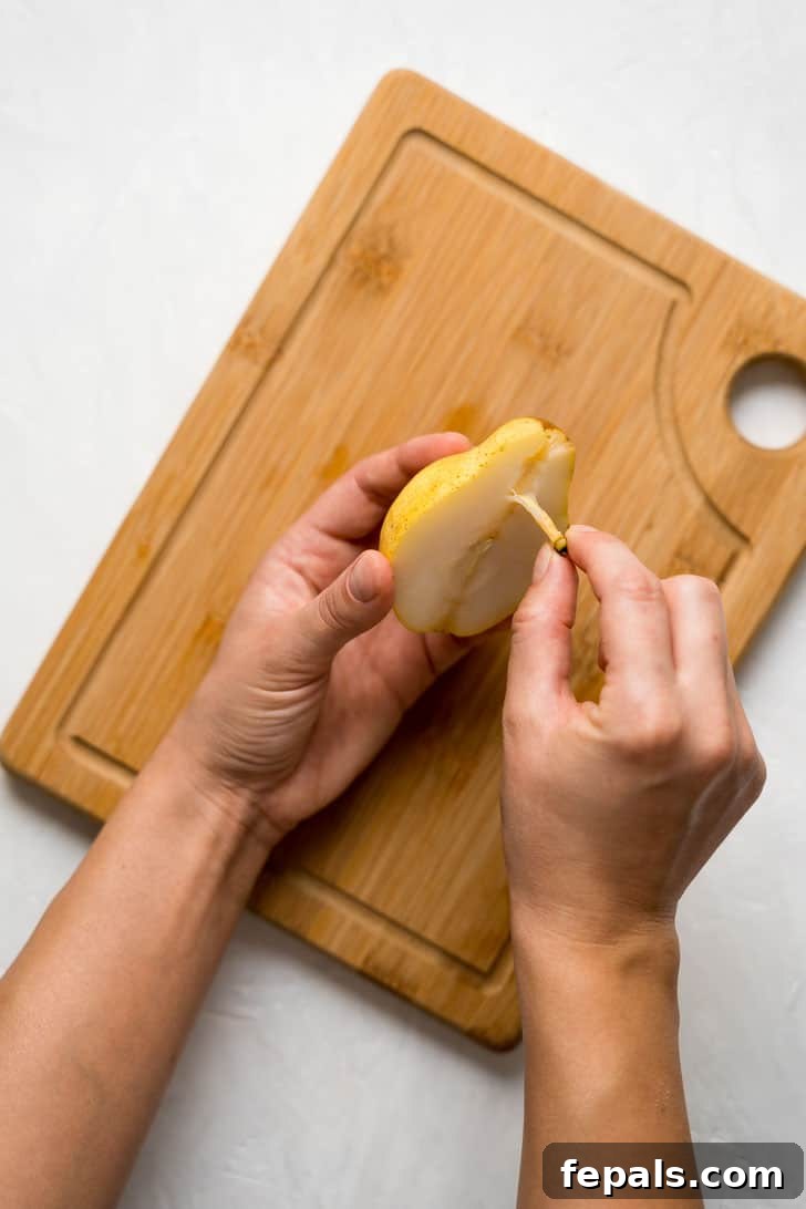 How to Cut a Pear Fancy A hand carefully pulls the stem from the top of a pear half, ensuring a clean cut.