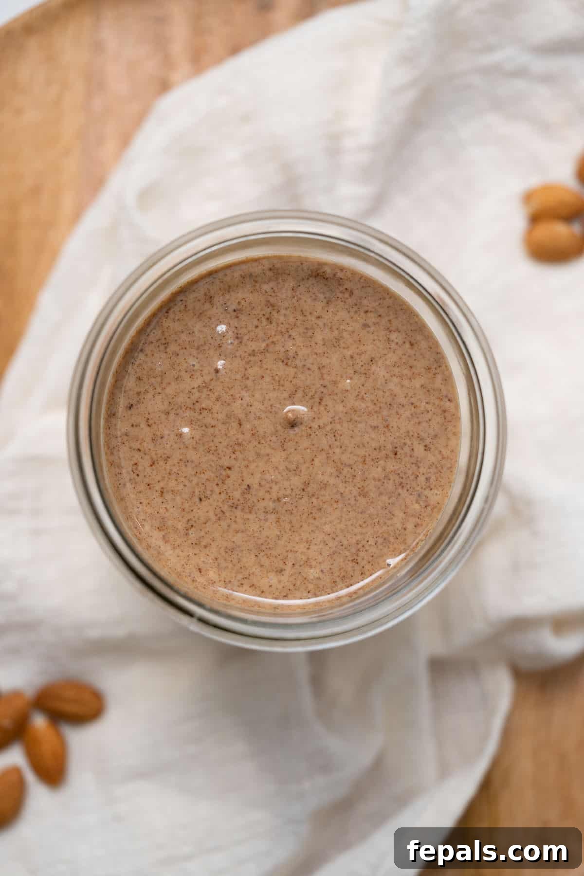 Homemade almond butter in a glass jar, resting on white linen, showcasing its creamy texture.