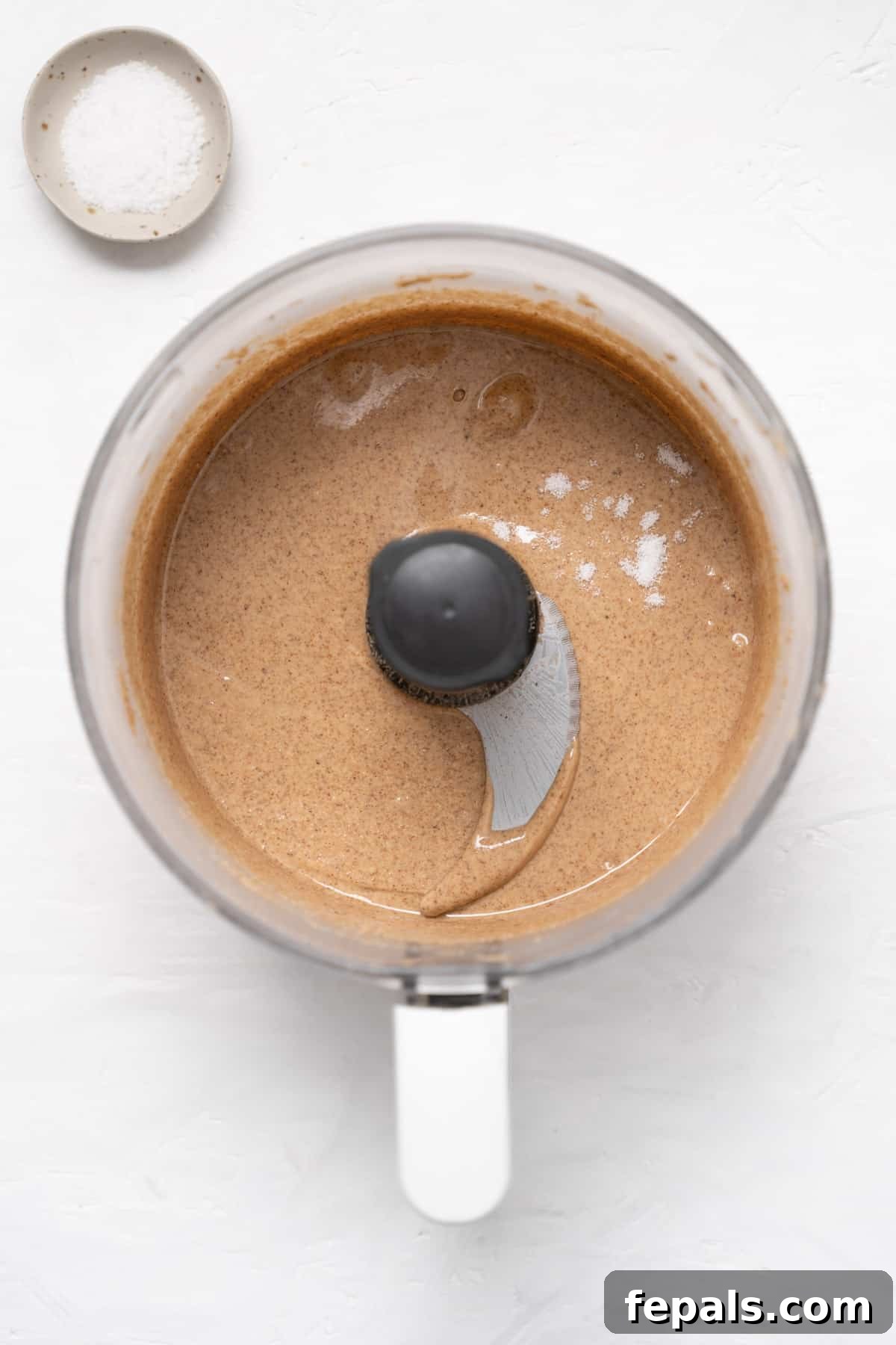 The fully blended and seasoned almond butter, now ultra-creamy and runny, in the food processor.