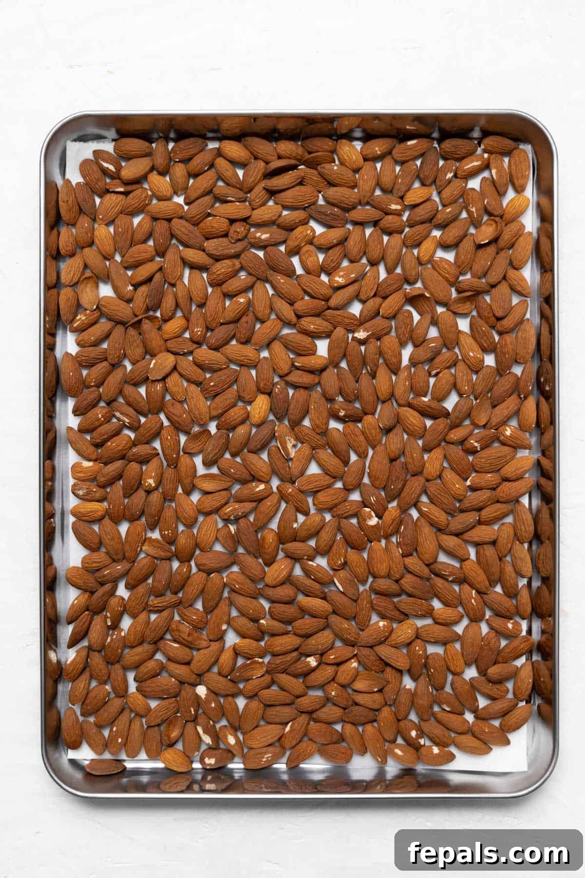 Raw almonds spread evenly on a baking sheet lined with parchment paper, ready for toasting.