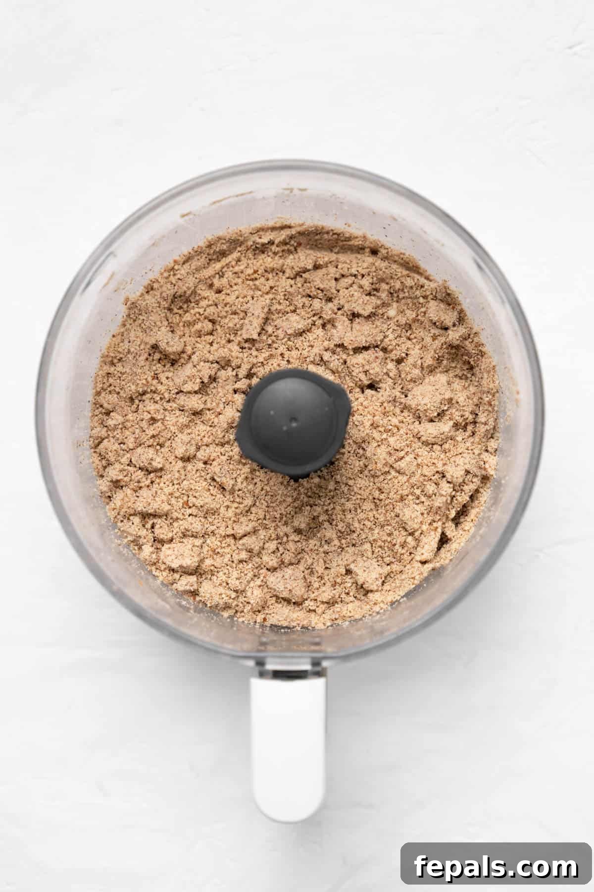 Top-down view of almonds after initial pulsing in a food processor, appearing as crushed pieces.