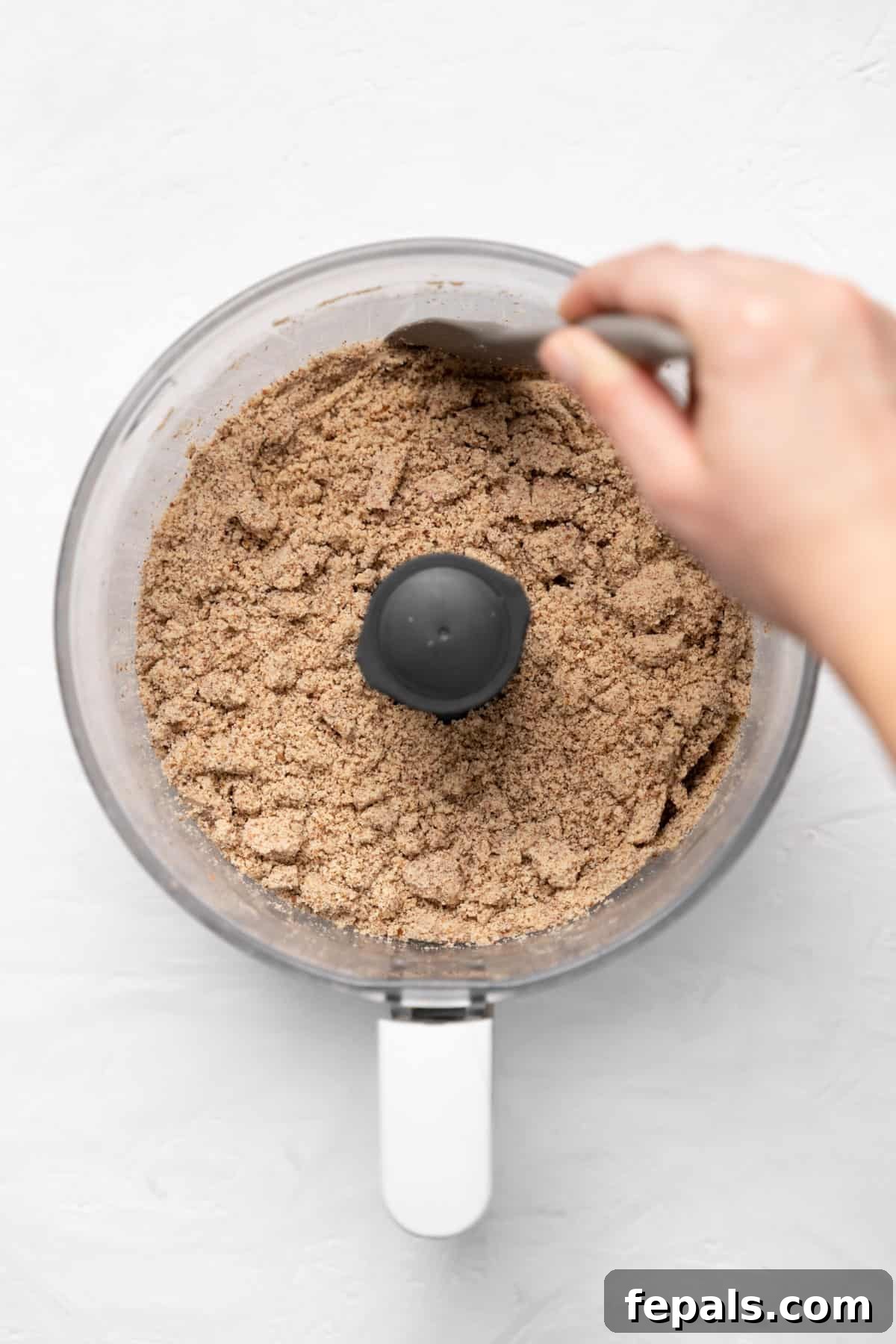 Almonds continuing to blend in a food processor, transitioning from coarse meal to a thicker paste.