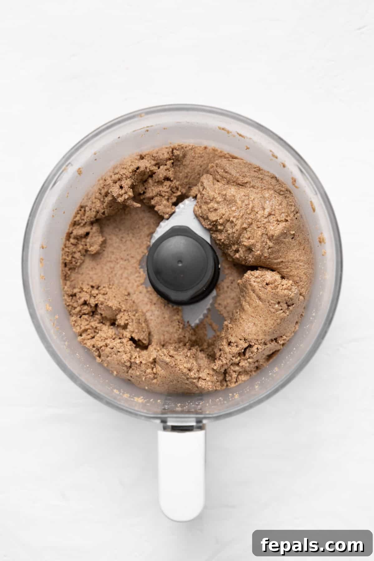 Almond butter blending in a food processor, showing the progression to a smoother, thicker consistency.