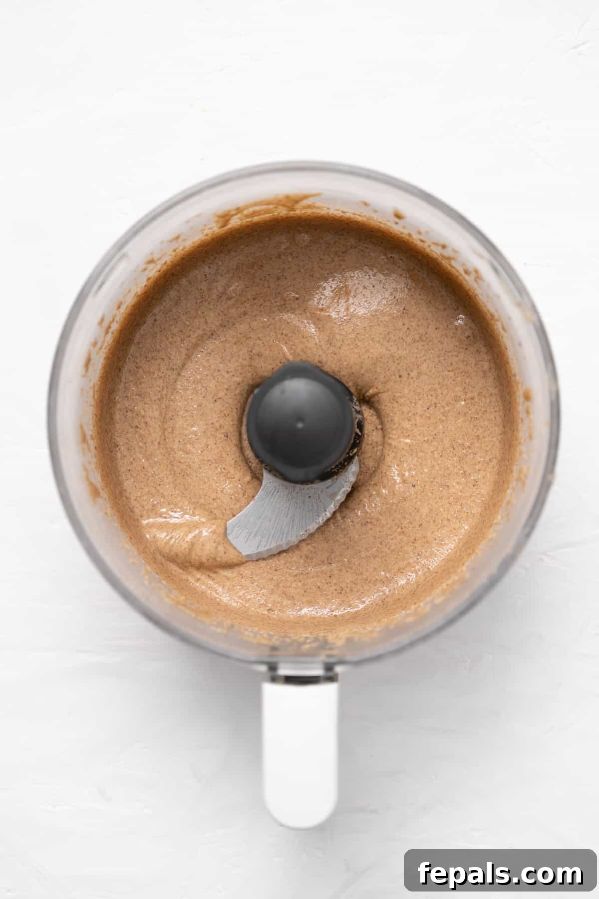 Almond butter actively processing in a food processor, becoming visibly smoother and more liquid.