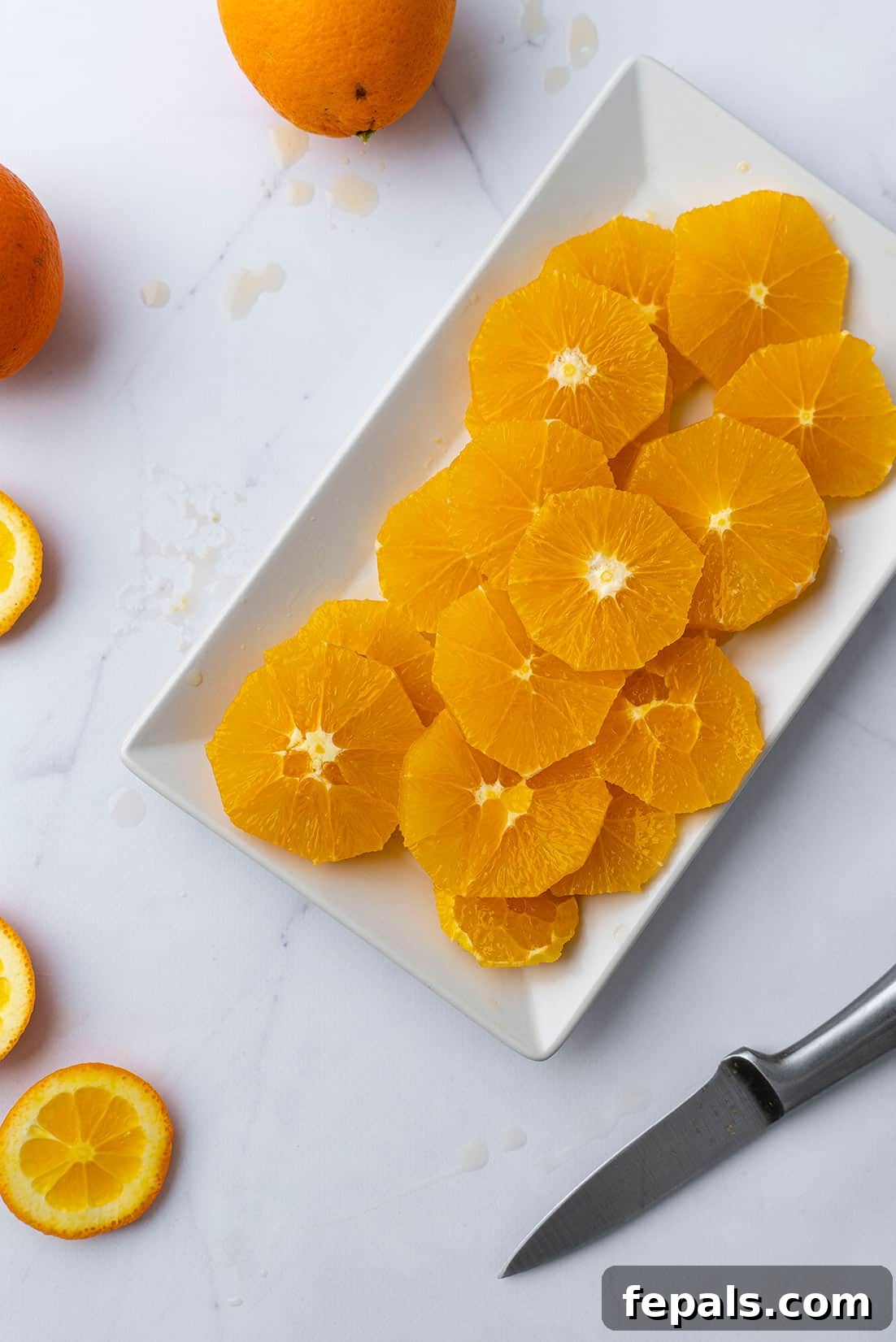 Bright orange slices neatly arranged on a white plate with a knife, ready to be enjoyed.