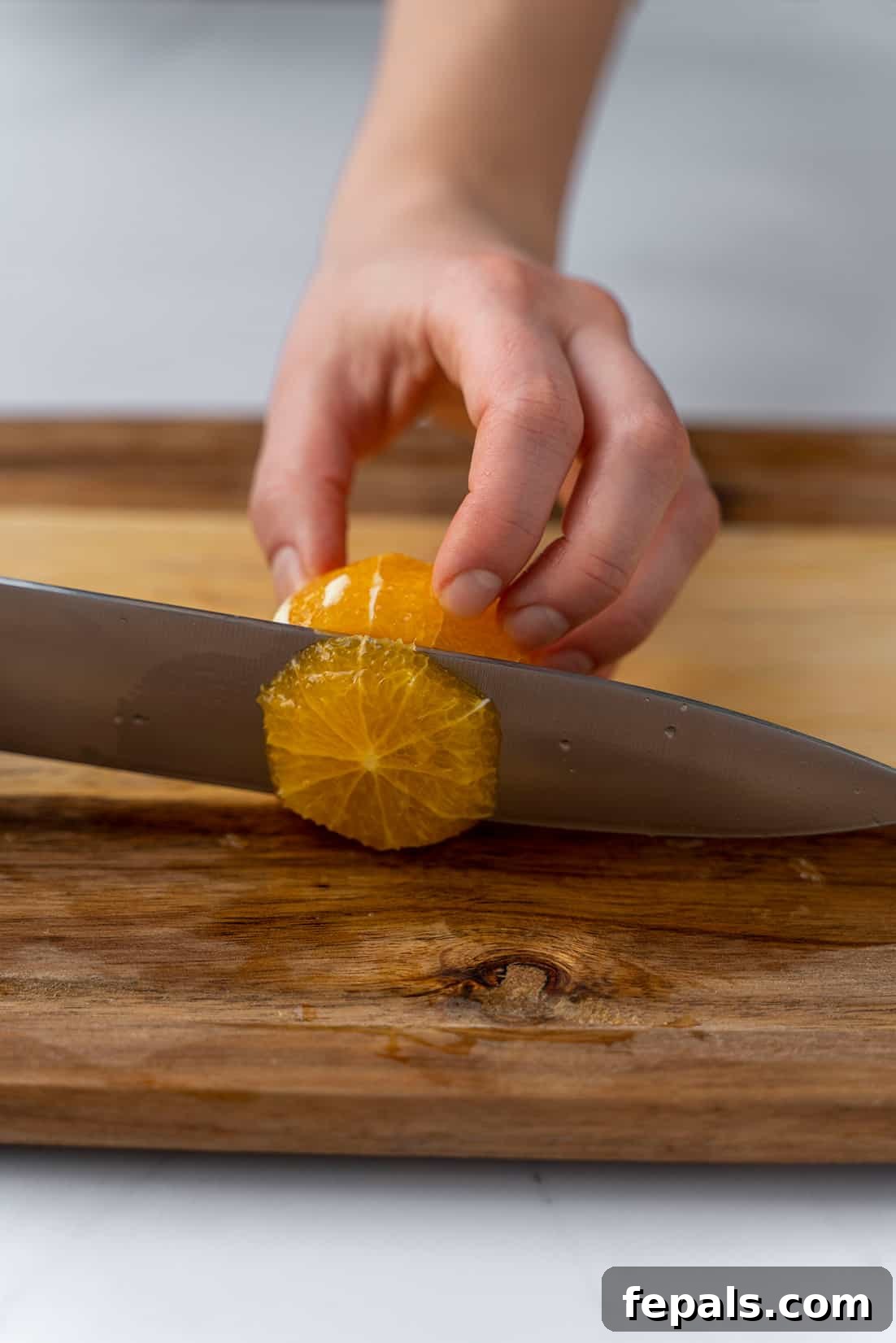 Slicing an already peeled orange into perfect circular rings with a knife on a cutting board.