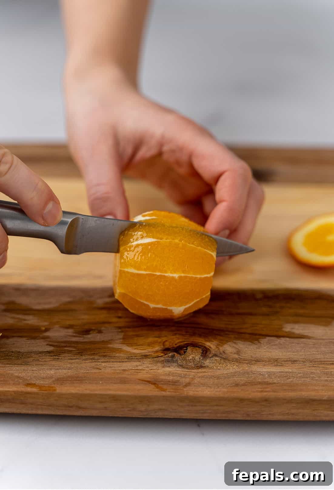 Slicing through the orange flesh with a knife on a cutting board, carefully separating a segment from its membrane.