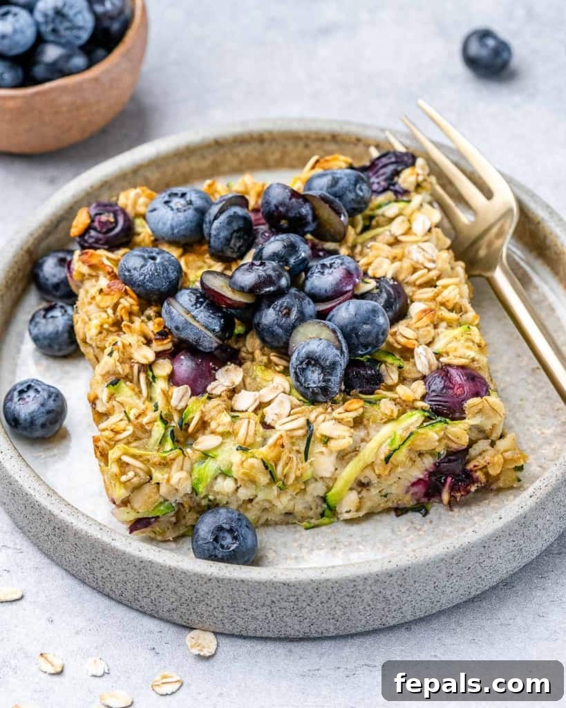 Slice of zucchini baked oatmeal with blueberries on a plate with a fork.
