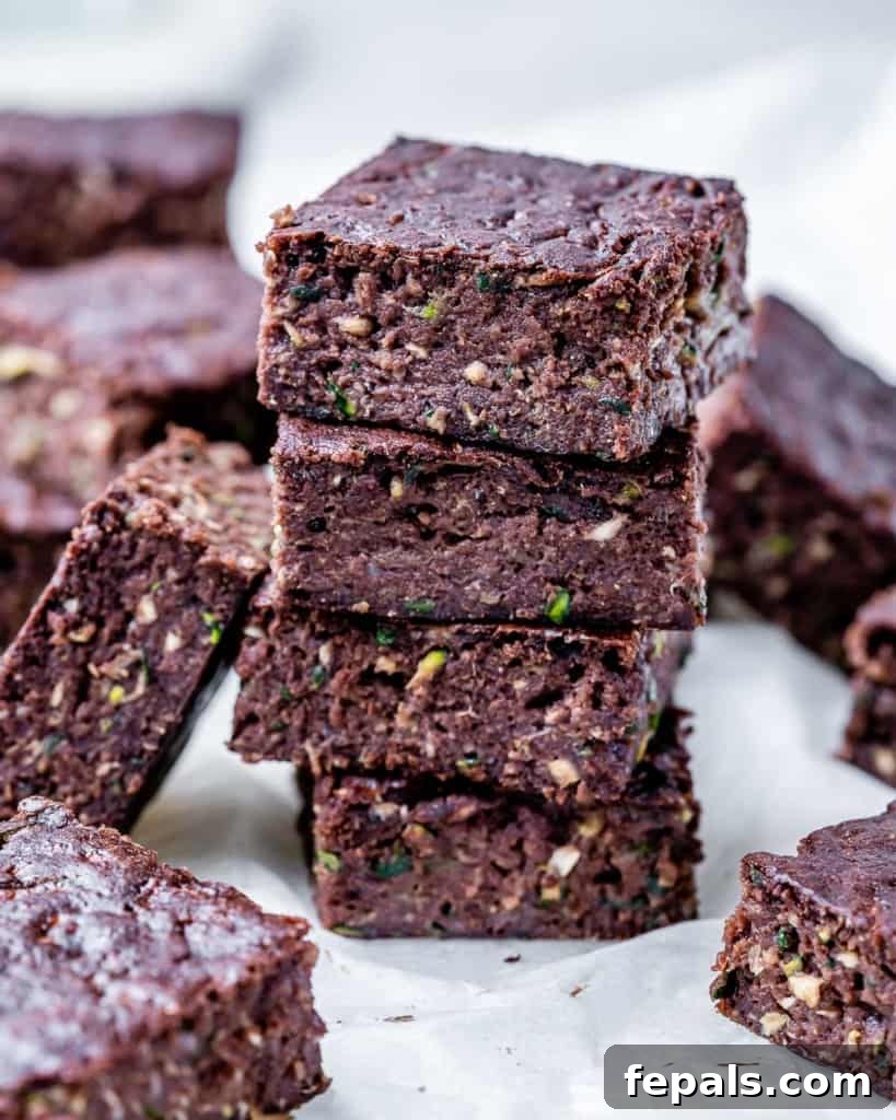 A stack of four perfectly square healthy zucchini brownies, showing off their dense, fudgy texture and rich chocolate color.