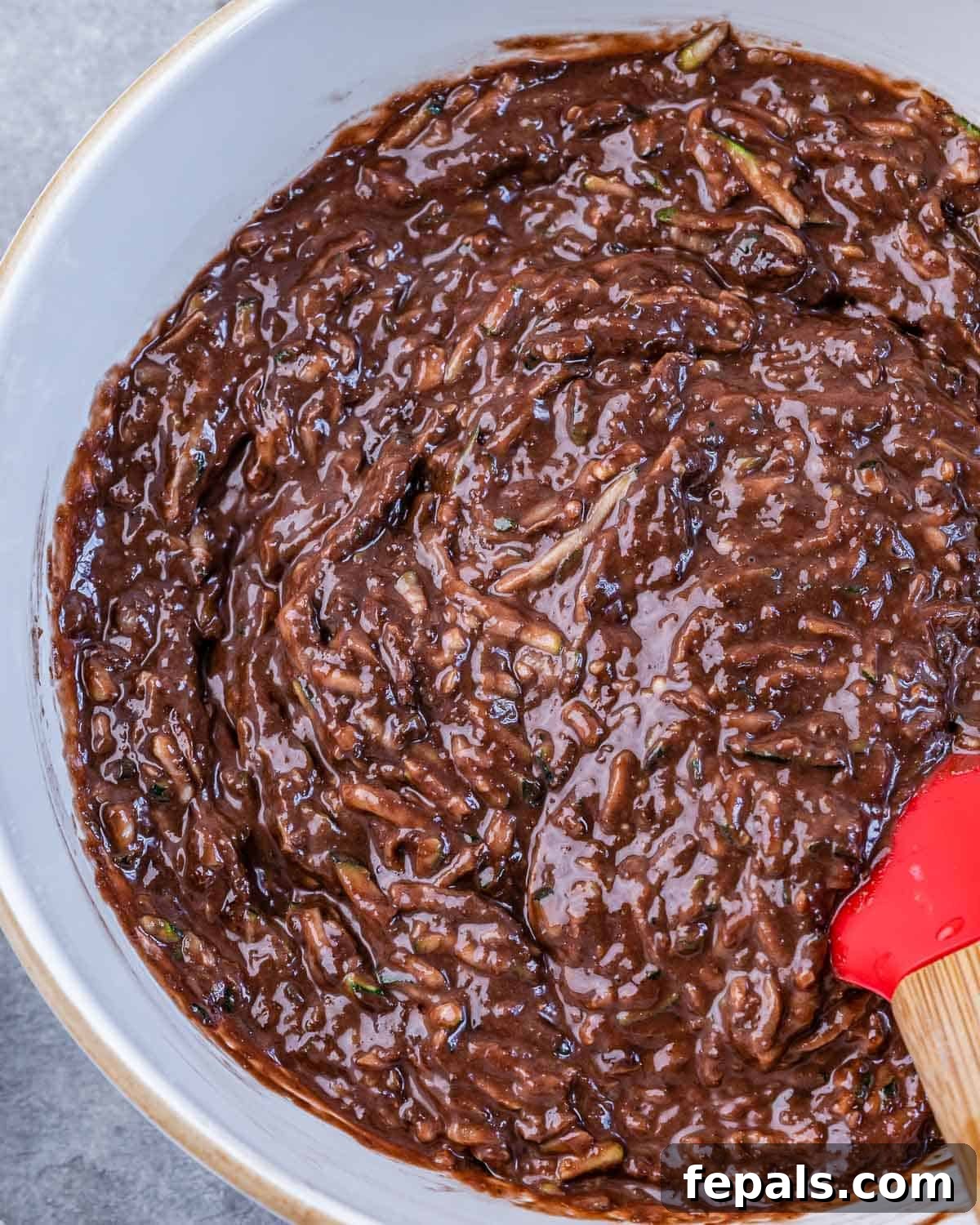 A hand stirring together the thick chocolate brownie batter in a large mixing bowl, showing the consistency before baking.