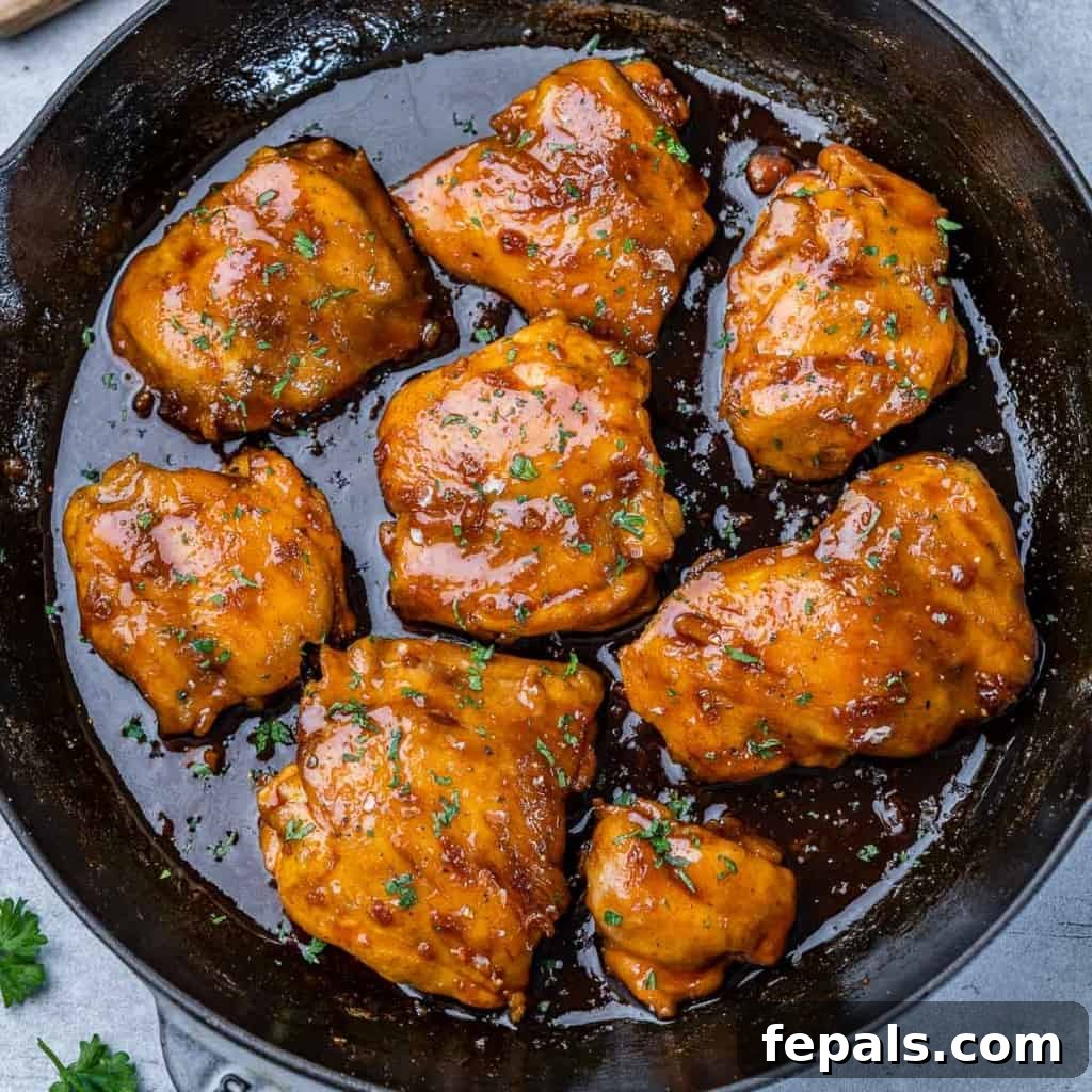 The Ultimate Chicken Adobo 2 Top-down view of beautifully seared adobo chicken thighs simmering in a rich, dark sauce in a black skillet.