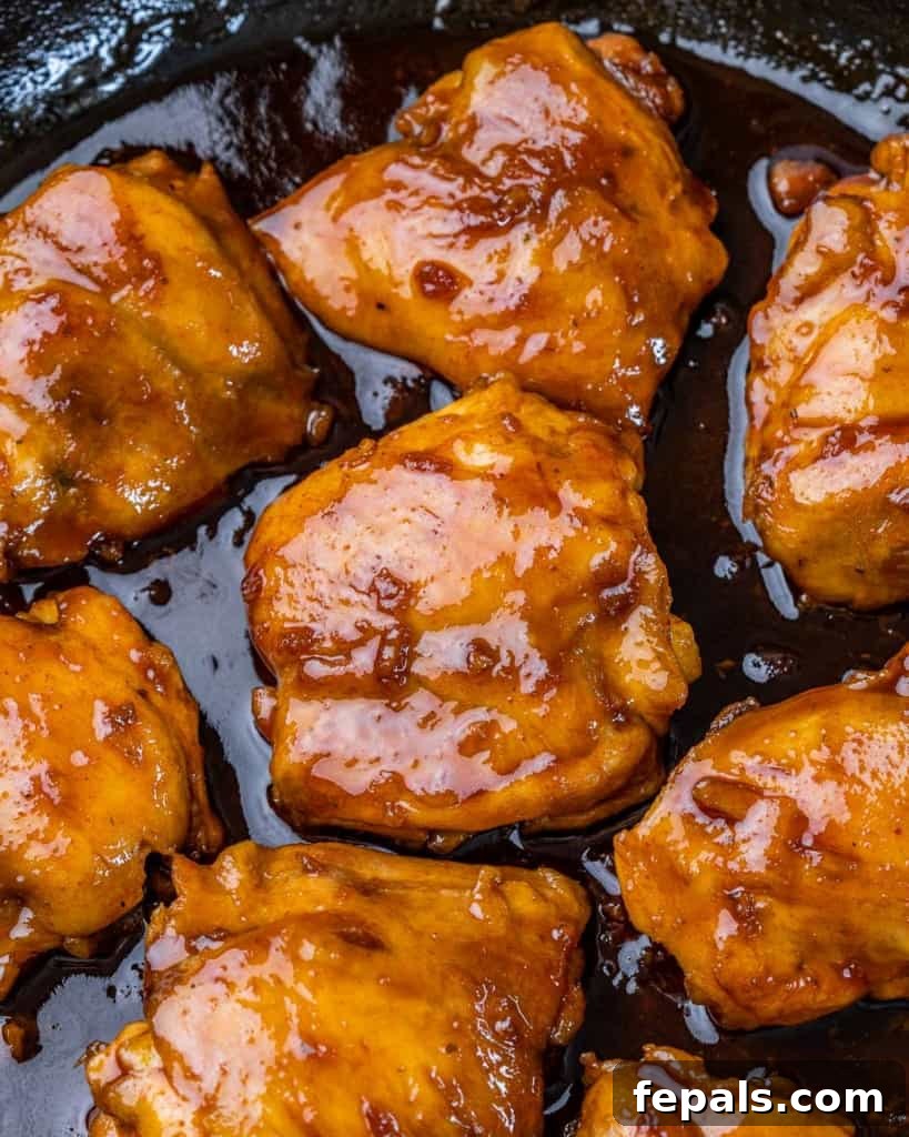 The Ultimate Chicken Adobo 3 Juicy chicken thighs bathed in a glossy, dark adobo sauce, simmering gently in a cast iron skillet.