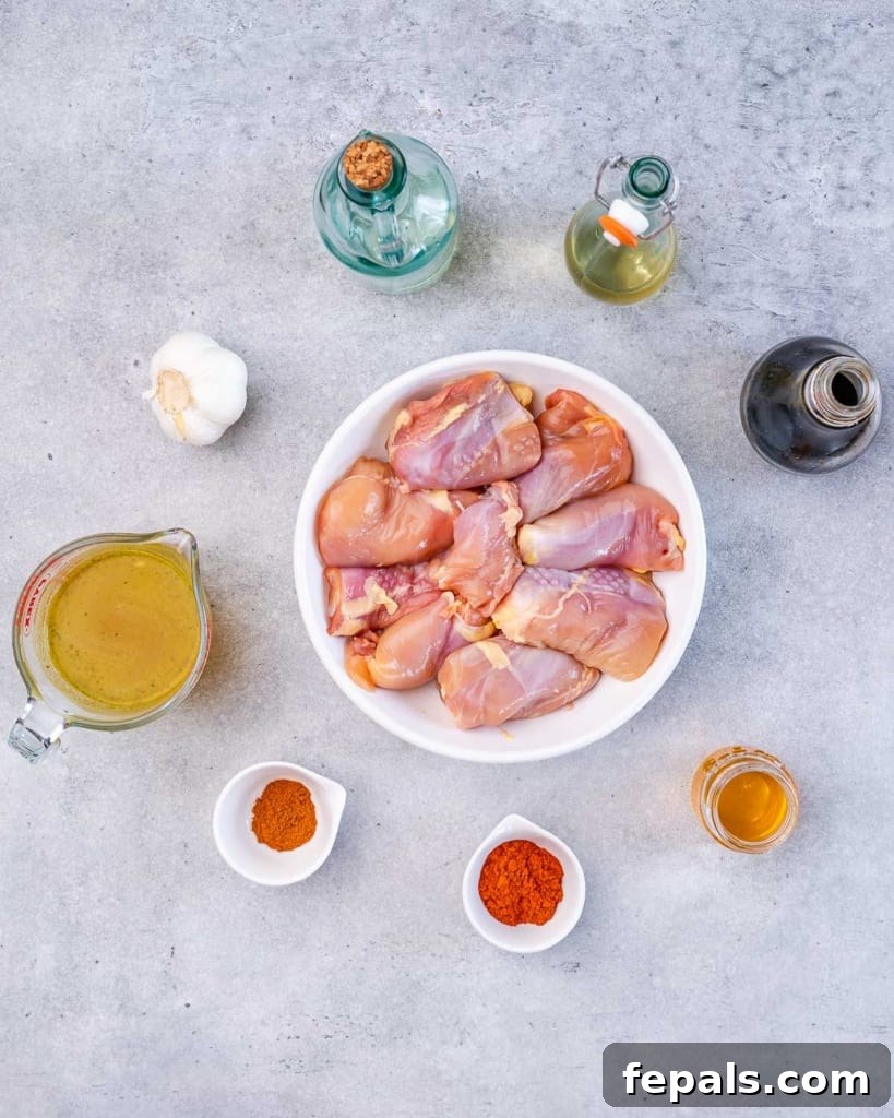 The Ultimate Chicken Adobo 4 A selection of raw chicken thighs on a plate, surrounded by small bowls containing various Adobo ingredients like garlic, vinegar, and honey.