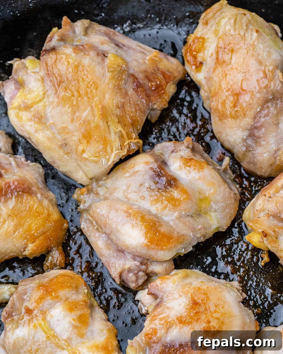 The Ultimate Chicken Adobo 5 Close-up shot of chicken thighs searing in a hot skillet, developing a golden-brown crust.