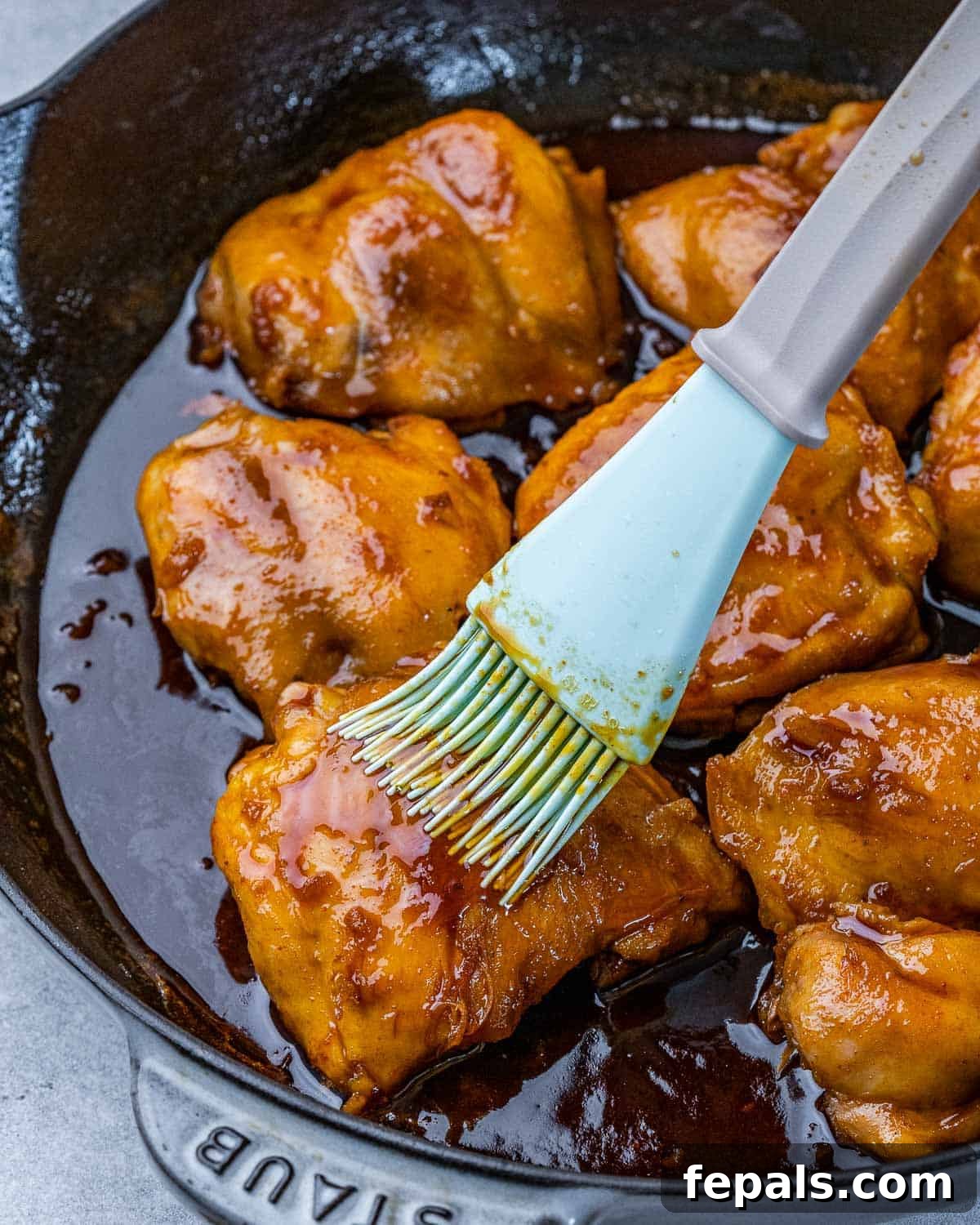 The Ultimate Chicken Adobo 6 A hand basting luscious adobo sauce over chicken thighs simmering in a skillet, creating a beautiful glaze.