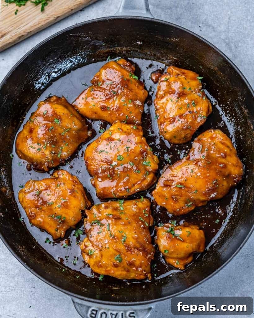 The Ultimate Chicken Adobo 9 Another top-down view of savory chicken thighs swimming in their rich adobo sauce within a black skillet, garnished with fresh herbs.