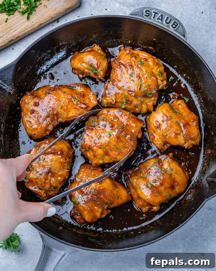 The Ultimate Chicken Adobo 10 Tongs lifting a piece of perfectly cooked Chicken Adobo from a skillet, ready to be served.