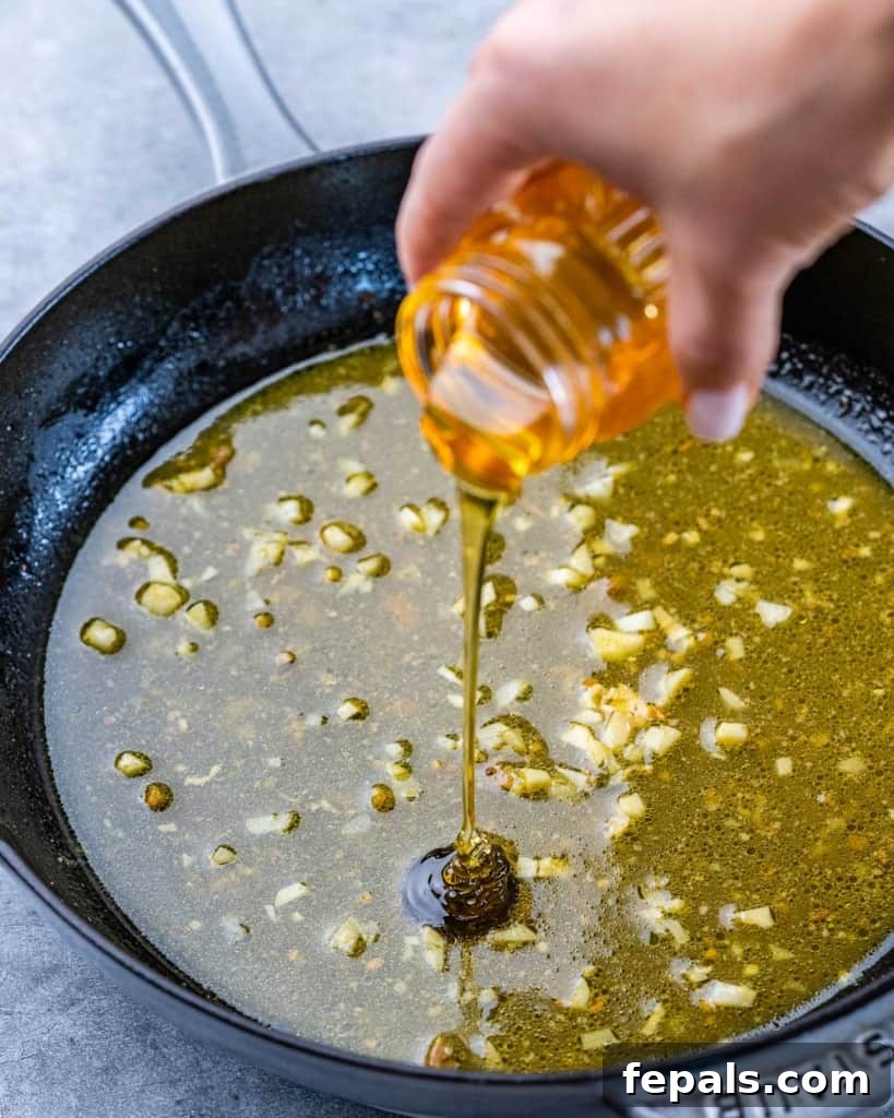 Effortless Baked Boneless Thighs 5 honey being poured onto a pan with sauteed garlic and broth