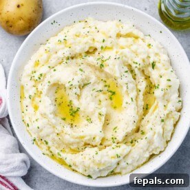 Mash potato on a white round plate topped with melted vegan butter and fresh herbs.