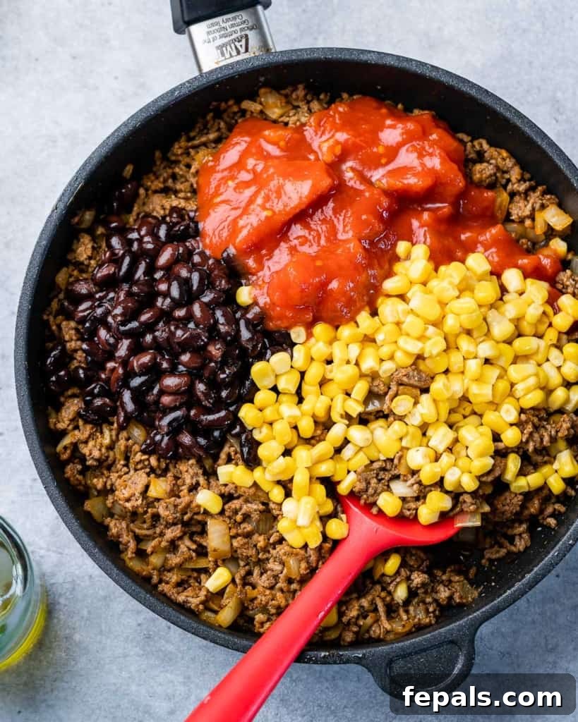 Ground beef, corn, and black beans simmering with crushed tomatoes in a large skillet, ready for assembly.
