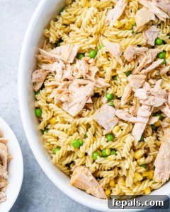 Cooked pasta, frozen peas, and corn mixed with flaked tuna in a white baking dish before sauce is added.