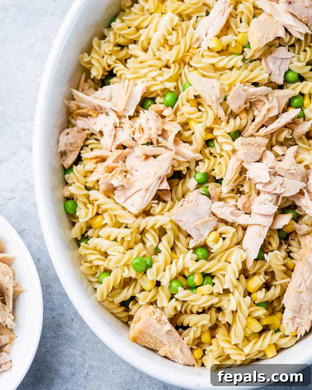 Wholesome Tuna Delight 6 Cooked pasta, frozen peas, and corn mixed with flaked tuna in a white baking dish before sauce is added.