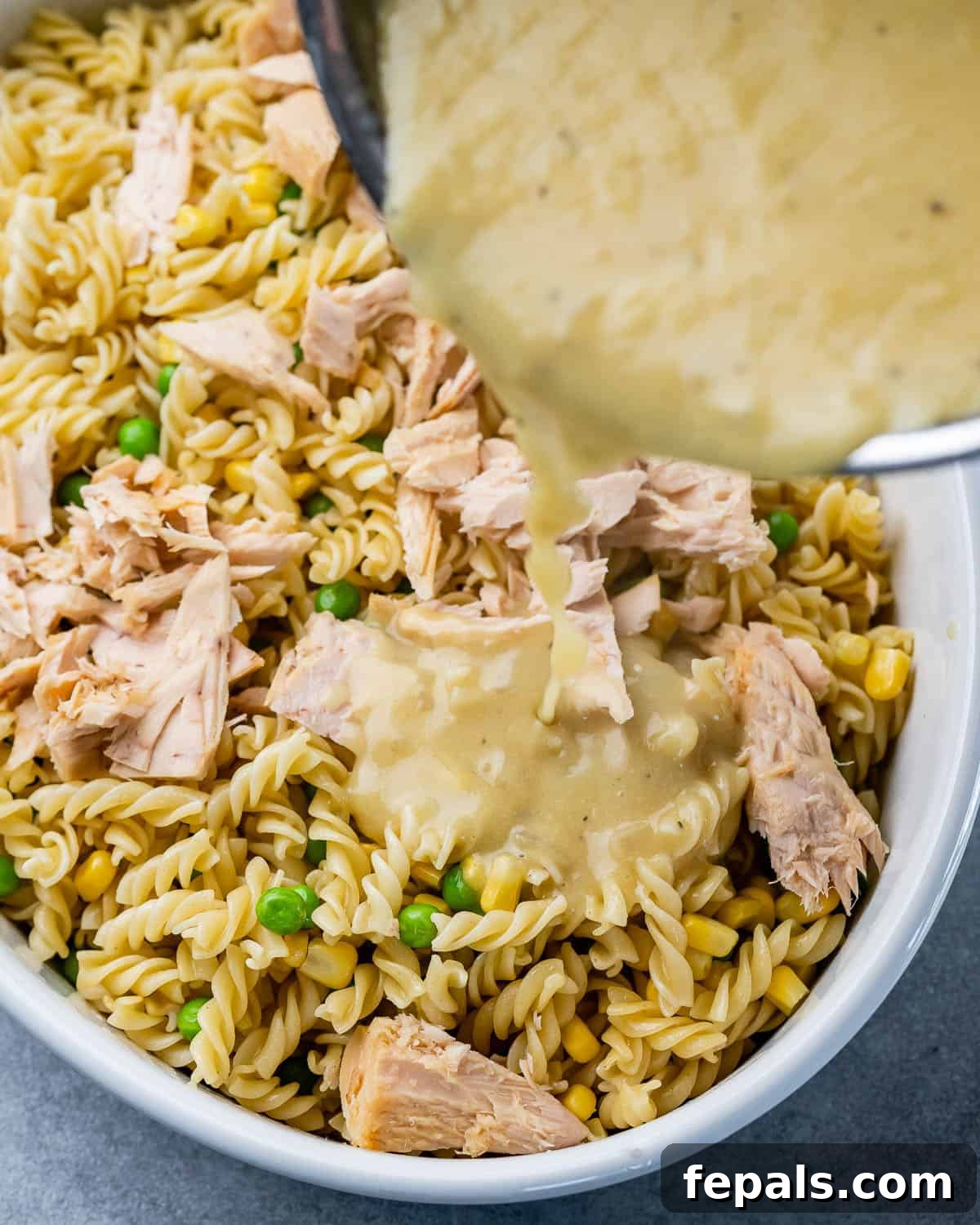 Wholesome Tuna Delight 7 Creamy cheese sauce being poured over the pasta, vegetables, and tuna mixture in a baking dish.