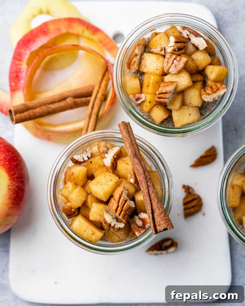 Spiced Apple Pie Chia Pudding 3 Top view of chia pudding in two jars over a cutting board with cinnamon sticks and chopped apples on the side of the pudding jar