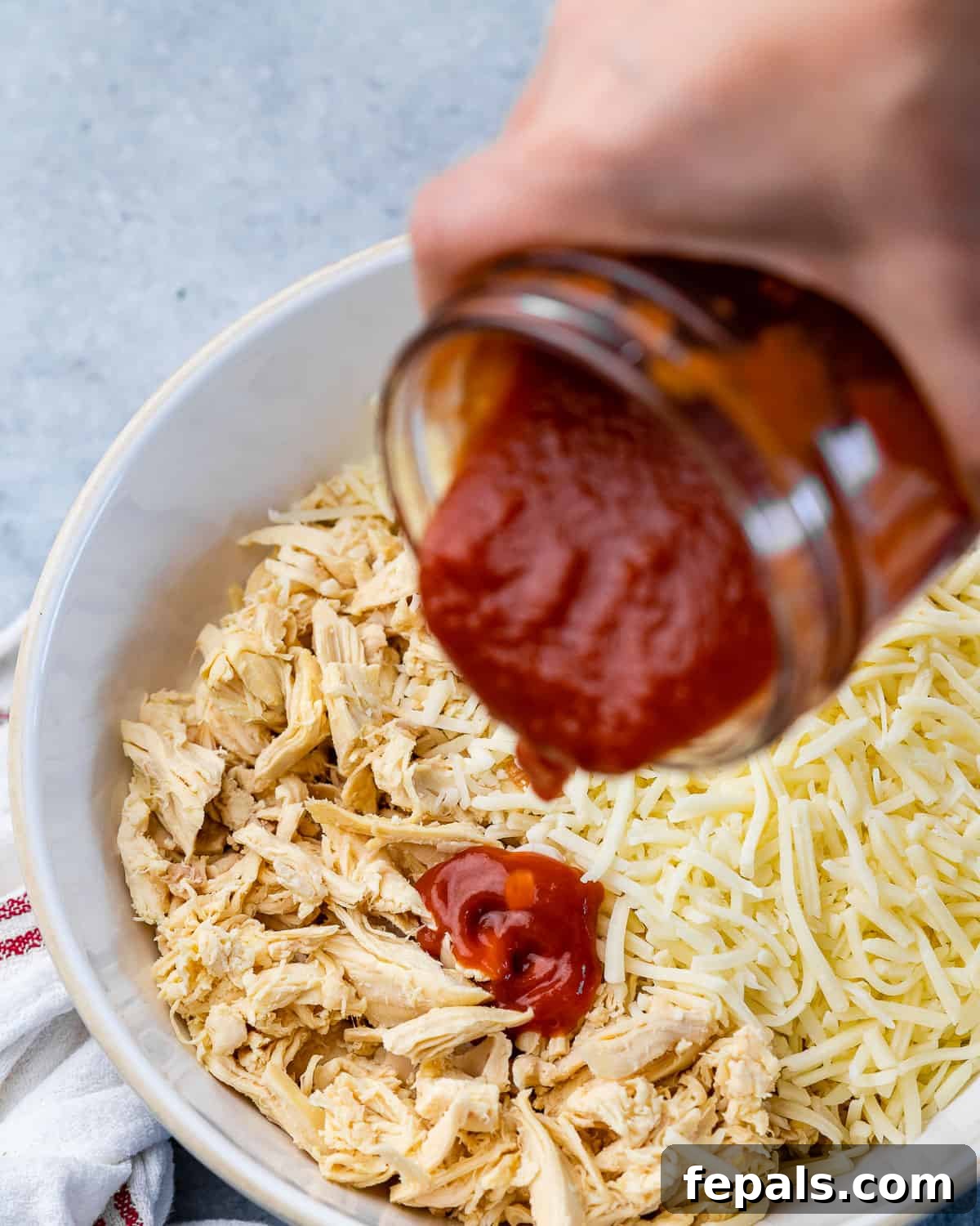Pouring enchilada sauce into bowl of shredded chicken. 