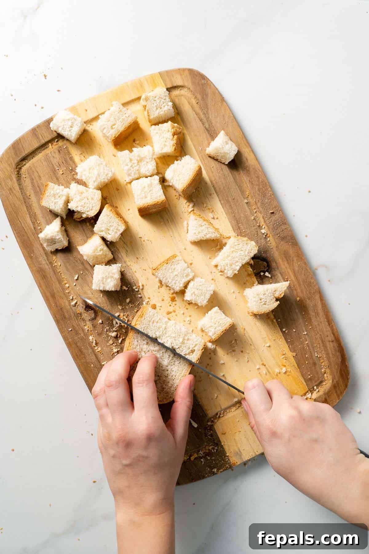 How To Make Croutons slicing sliced bread into cubes with knife on top of wooden cutting board