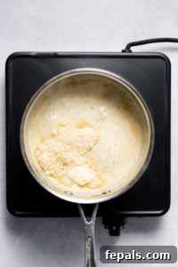 Adding parmesan cheese to homemade Alfredo Sauce for the final touch.
