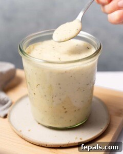Woman's hand spooning Alfredo Sauce from a glass jar, ready to be served.