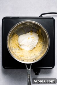 Adding cream cheese into pot with garlic and flour mixture to make the sauce.