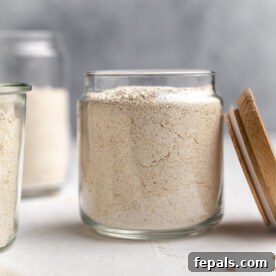 Side shot of fine oat flour inside a glass jar, with its lid placed to the right.