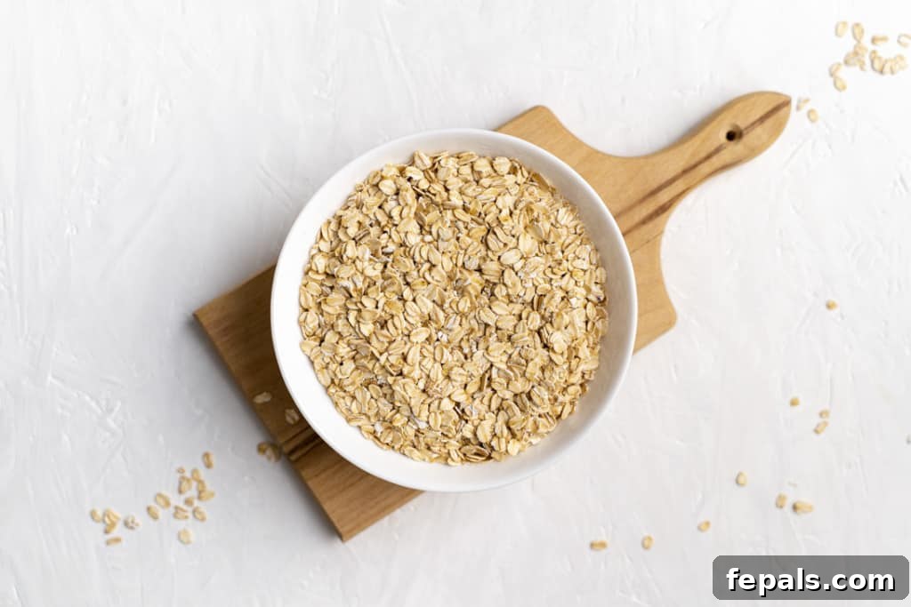 A clean white bowl brimming with old-fashioned rolled oats, resting on a rustic wooden cutting board, ready to be processed into flour.