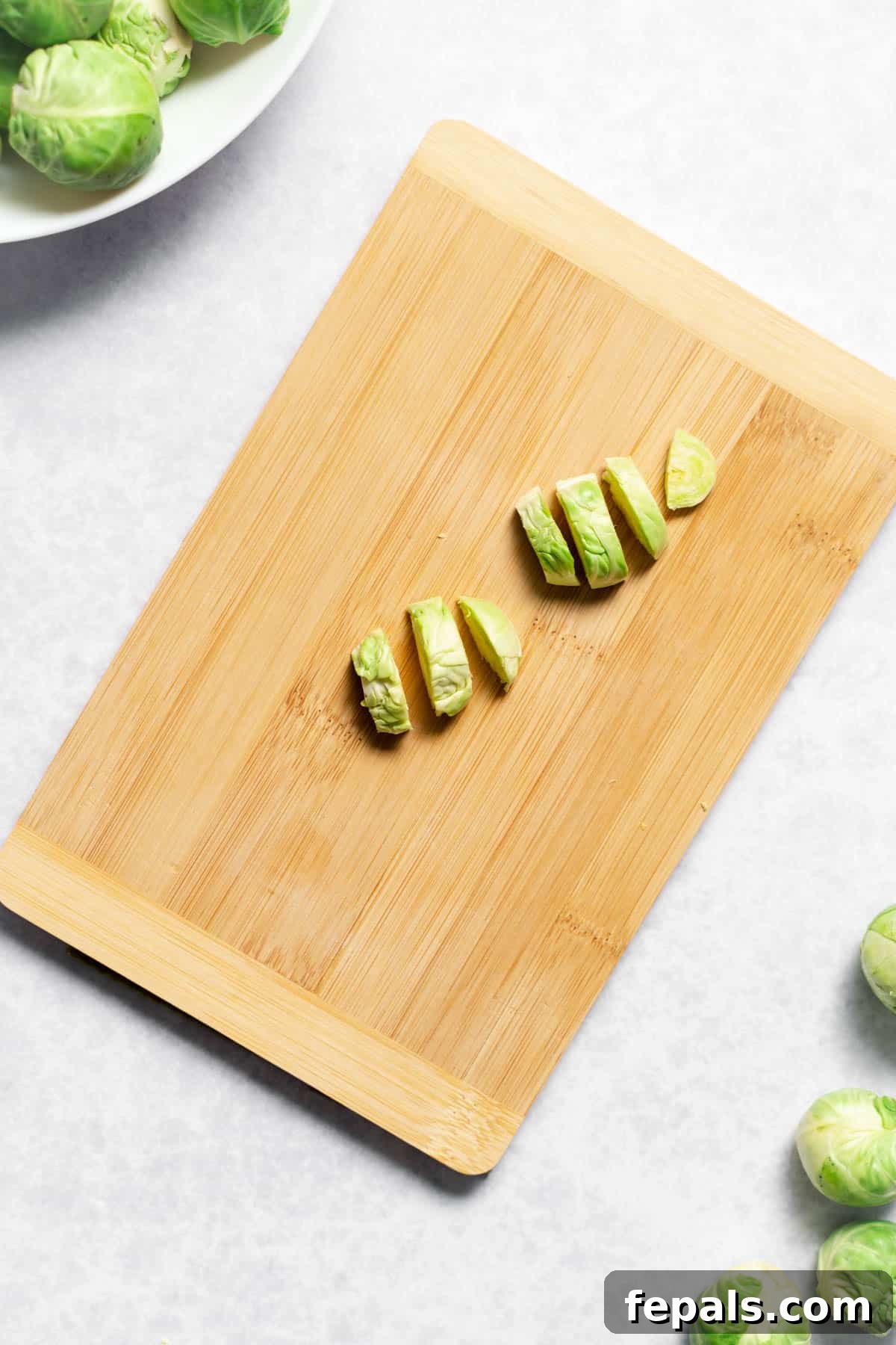 How To Cut Brussels Sprouts Piles of thinly sliced Brussels sprouts on a wooden cutting board