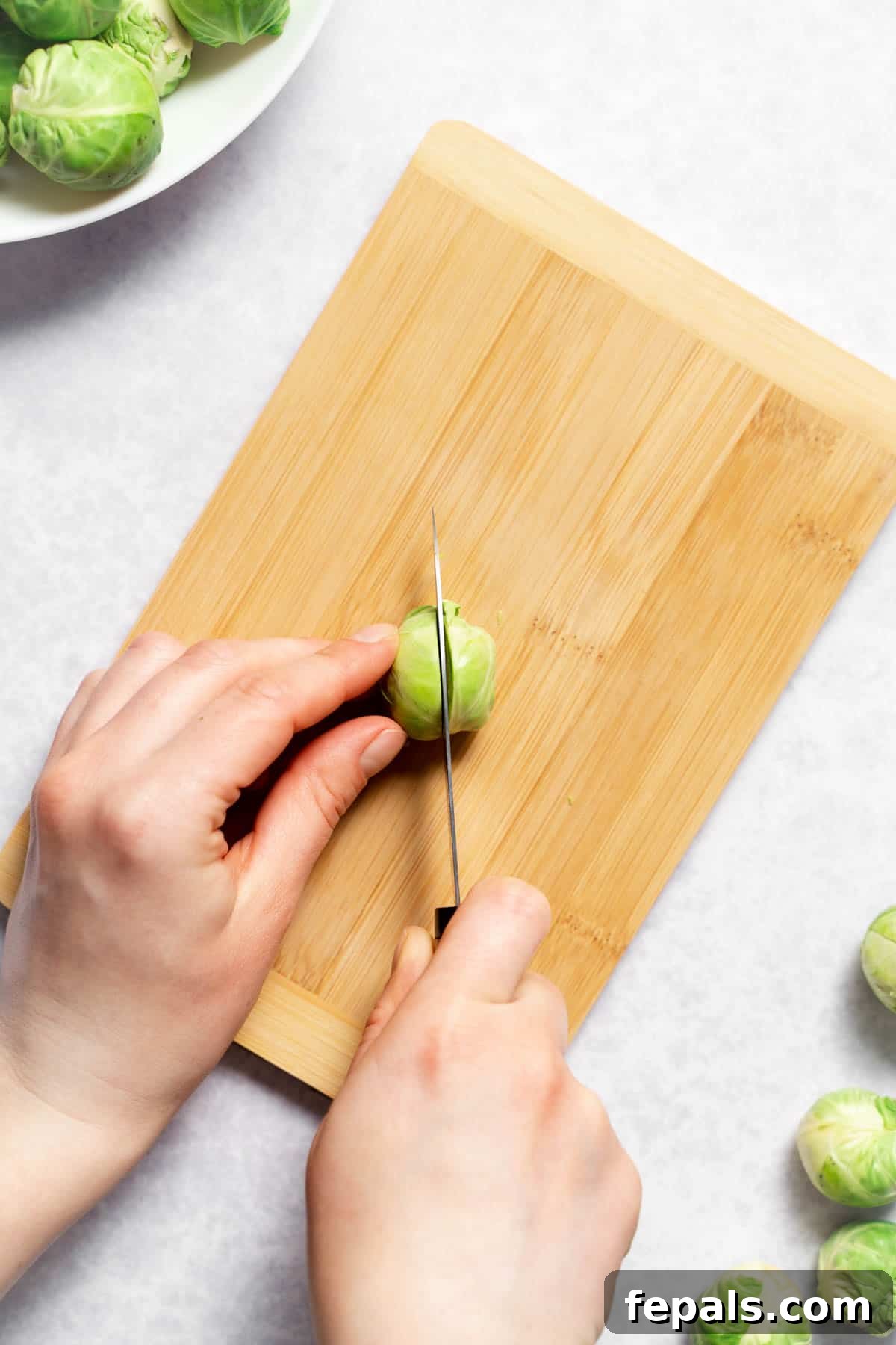 How To Cut Brussels Sprouts Vertically slicing a Brussels sprout in half with a chef's knife on a wooden cutting board