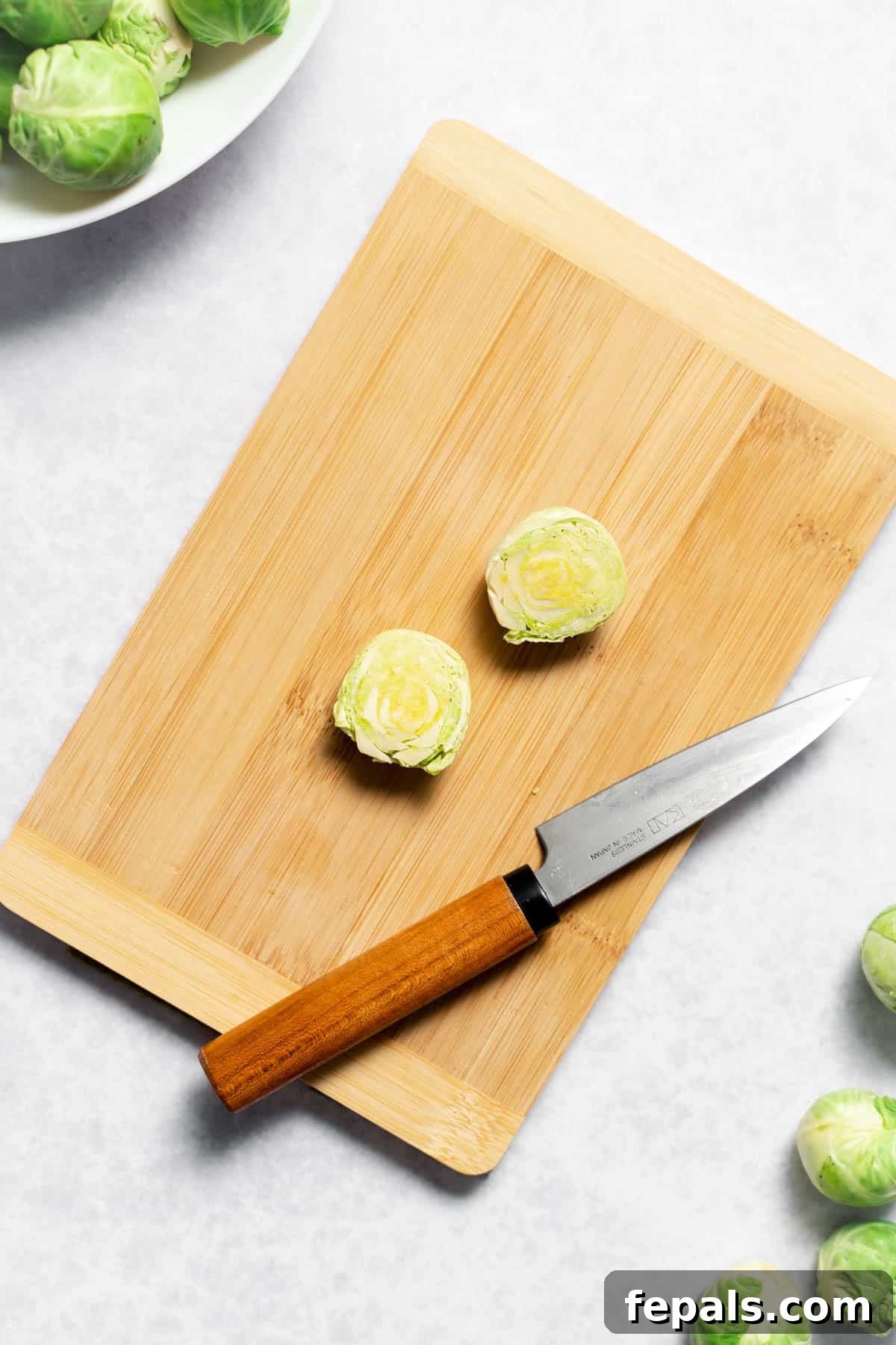 How To Cut Brussels Sprouts Two perfectly halved Brussels sprouts on a cutting board next to a knife