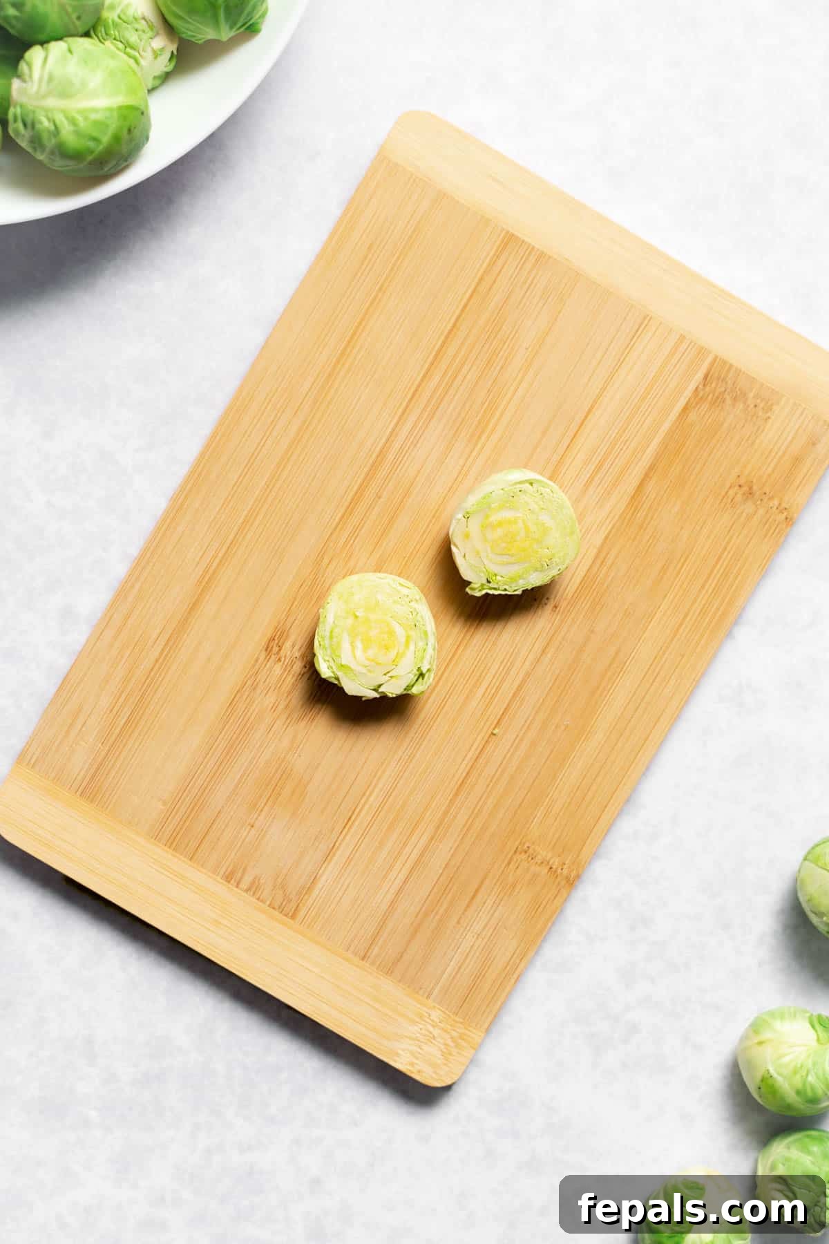 How To Cut Brussels Sprouts Two halves of a Brussels sprout on a cutting board, ready to be quartered