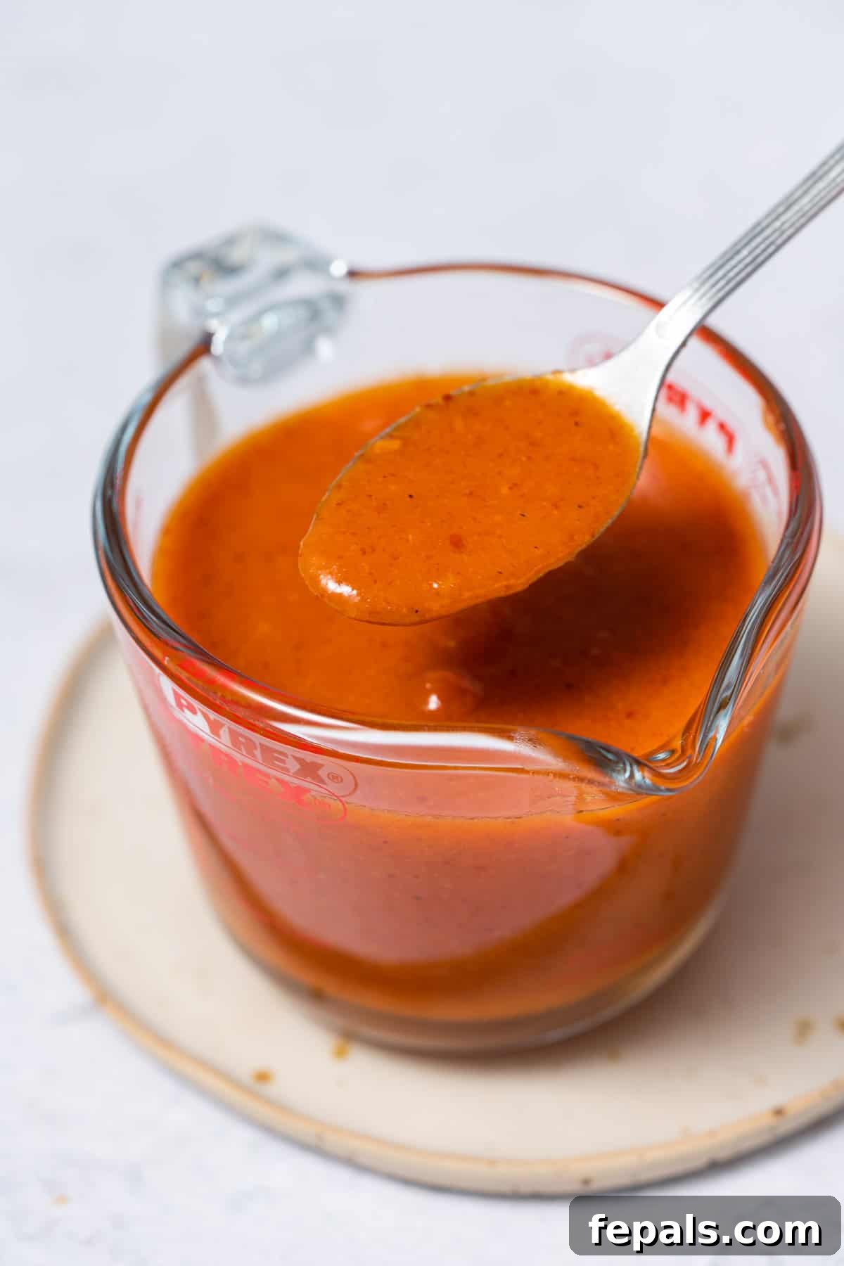 A spoon overflowing with glossy, vibrant homemade buffalo sauce, showcasing its smooth texture.
