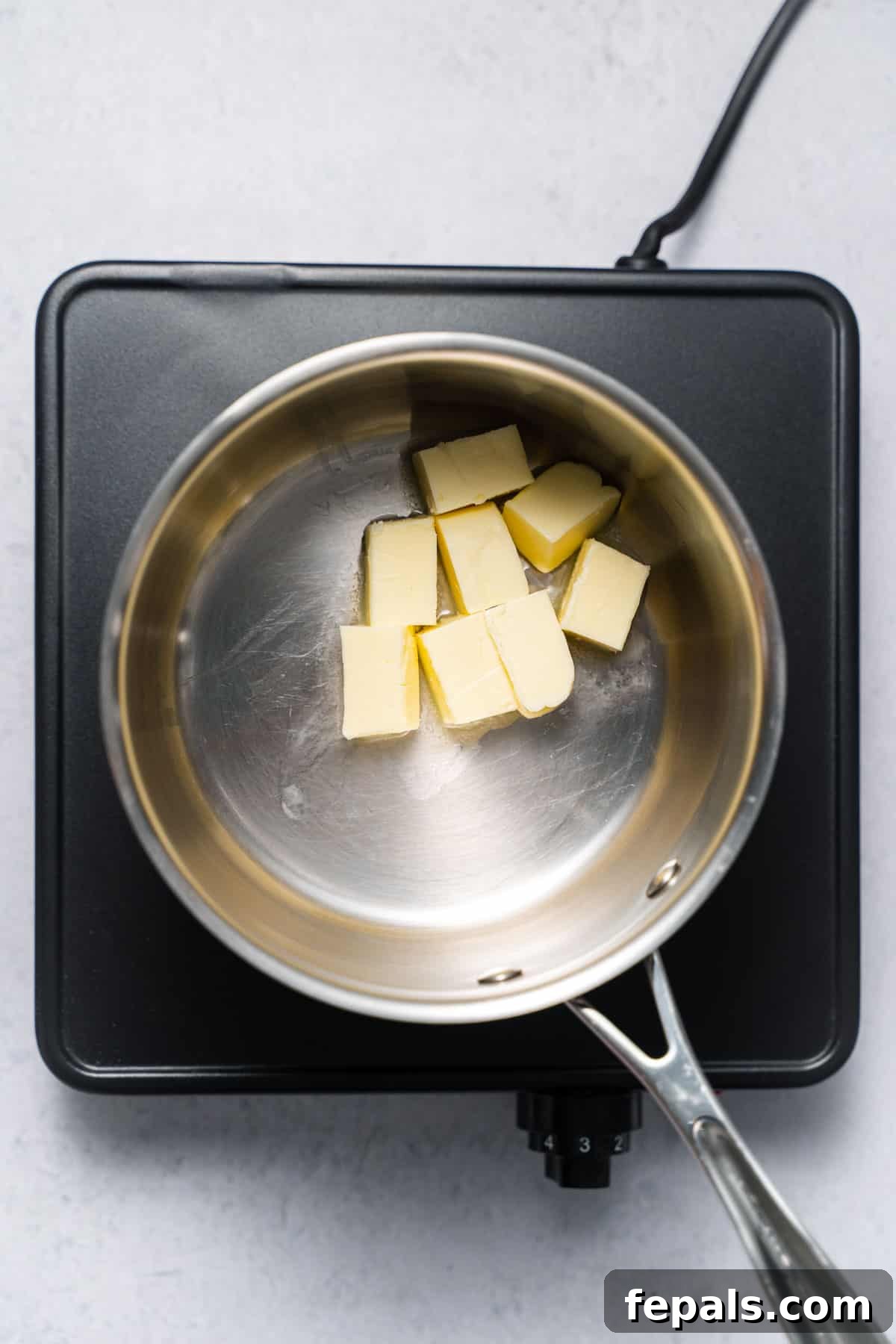 A small saucepan on a stovetop with cubes of butter melting gently, just beginning to liquify.
