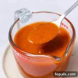 Side shot of buffalo sauce in a jar with a spoonful of sauce, showcasing its rich color and texture.