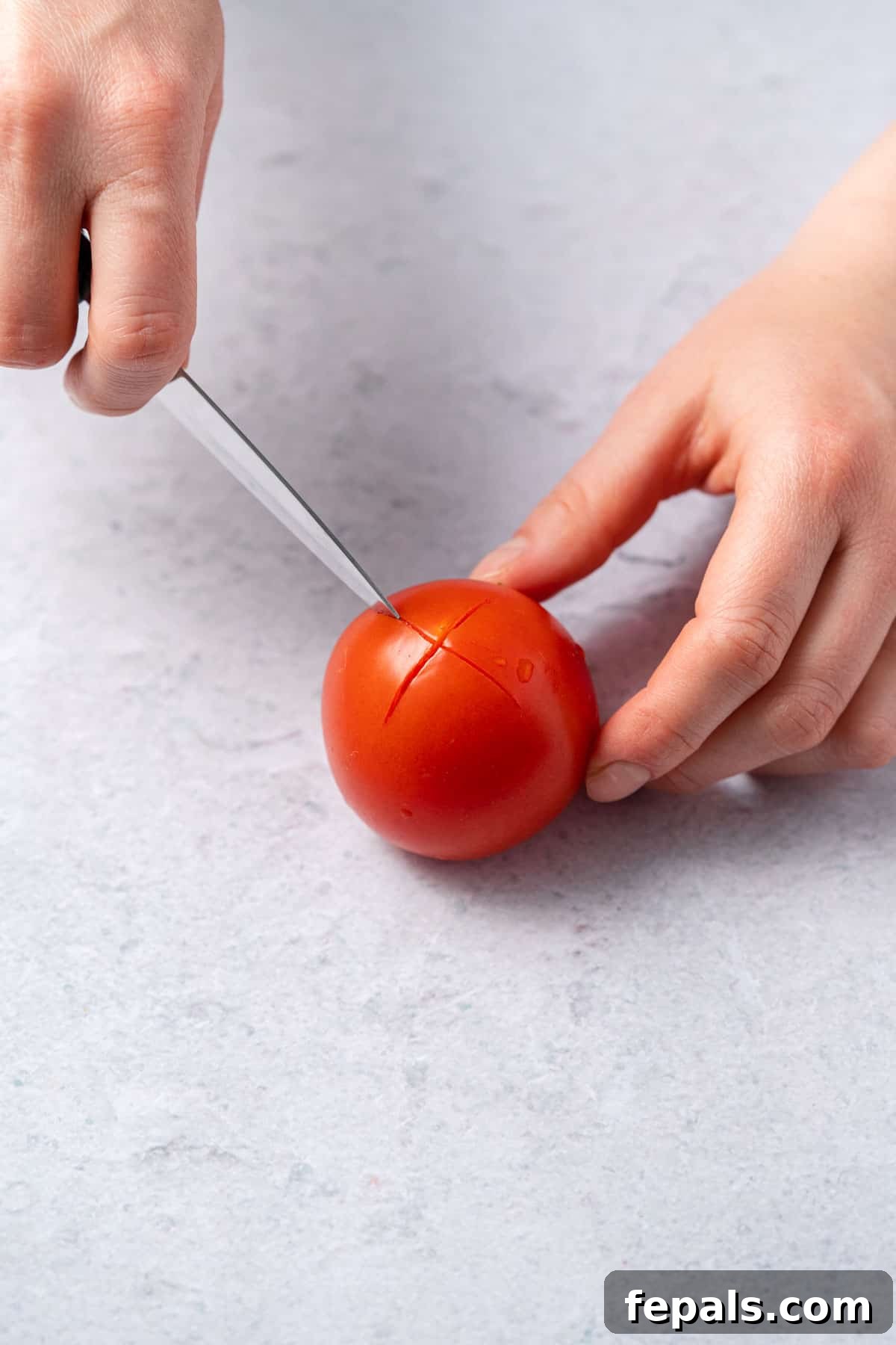 The Simple Trick to Perfectly Peeled Tomatoes 4 A close-up shot of a tomato with a small 'X' cleanly cut into its bottom, indicating preparation for blanching.