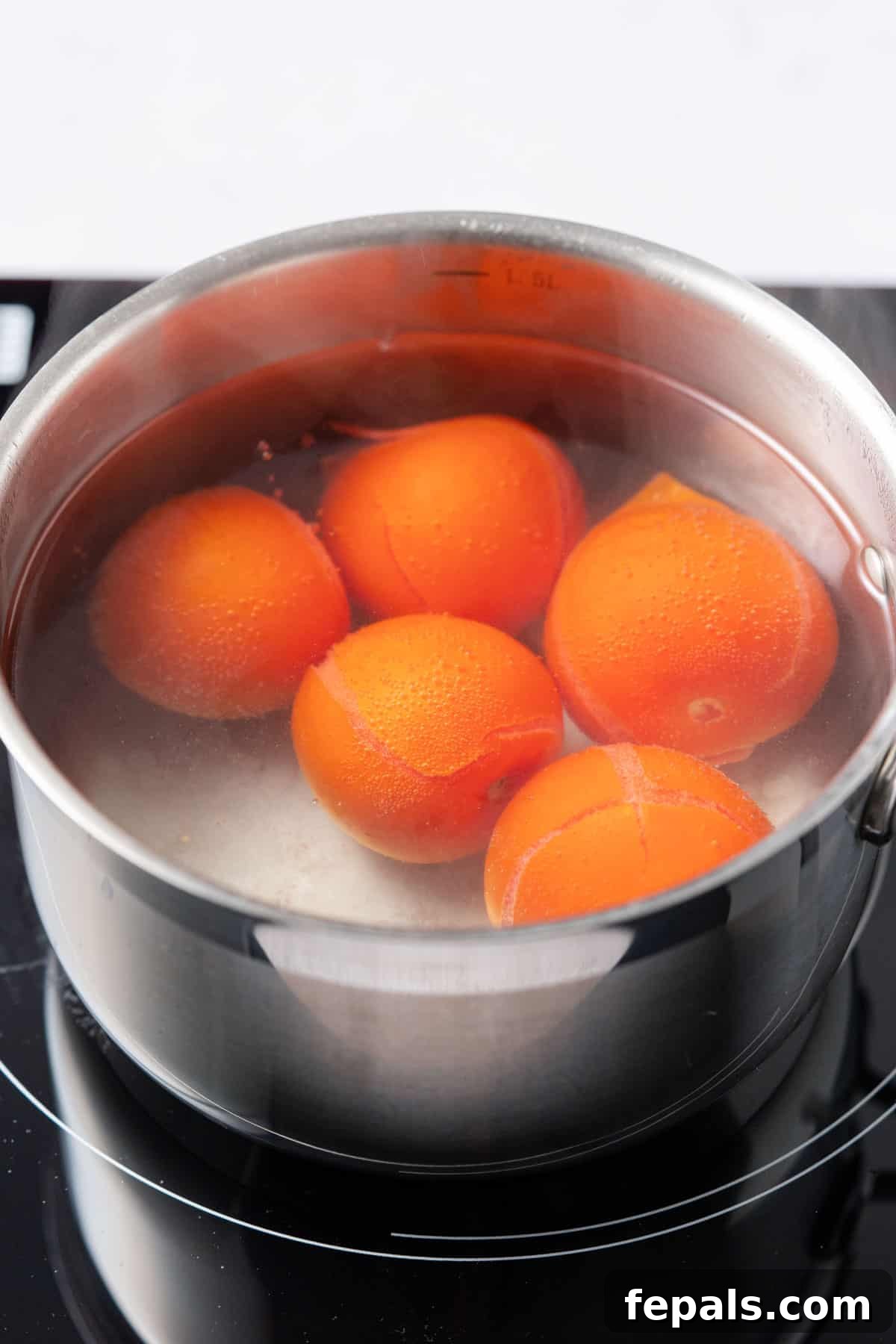 The Simple Trick to Perfectly Peeled Tomatoes 6 A view of five tomatoes gently boiling in a pot of water, their skins visibly starting to wrinkle and split.